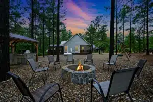 Airbnb near me in Broken Bow: twilight backyard with stone fire pit, outdoor seating, and illuminated cabin among pines at