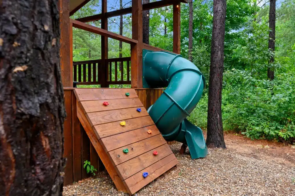 Turquoise slide and colorful climbing wall on a wooden deck among trees at a top rated Airbnb in Broken Bow, OK