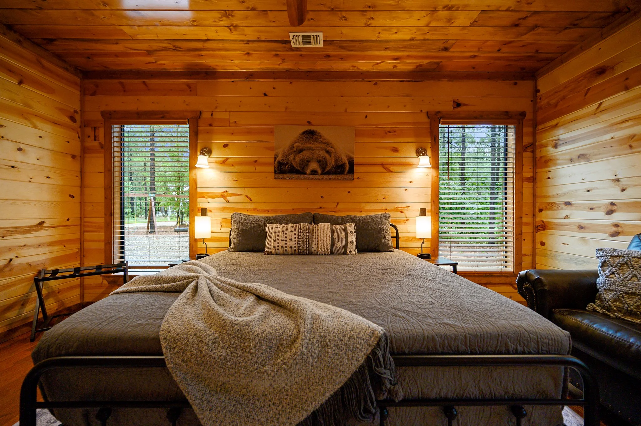 Rustic cabin bedroom with knotty pine walls, queen bed between large windows framing forest views, Endless Skyway Cabin near