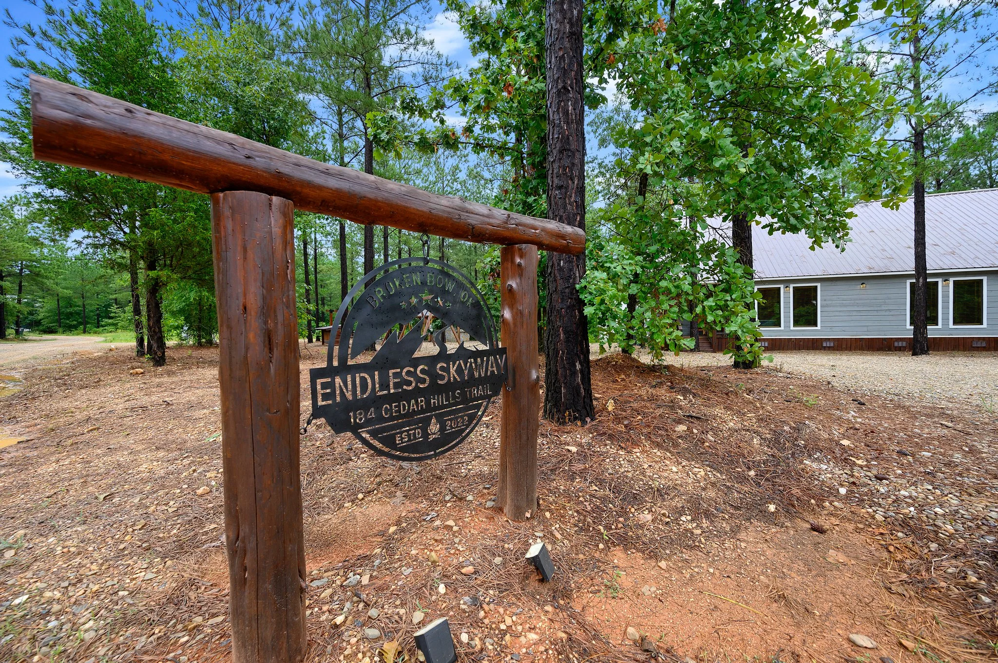 Rustic wooden entrance sign with dark circular metal plaque on timber posts at Endless Skyway Cabin, Broken Bow OK, near