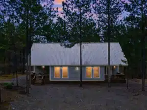 Modern cabin exterior at dusk with metal roof and glass doors among pine trees, a Broken Bow Oklahoma hotels alternative at