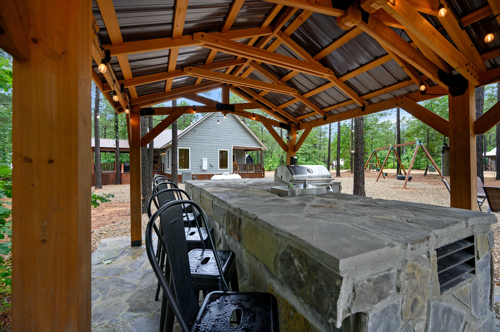 Covered timber-beam patio with concrete bar counter, black seating, and built-in grill at a Broken Bow, OK cabin by Endless