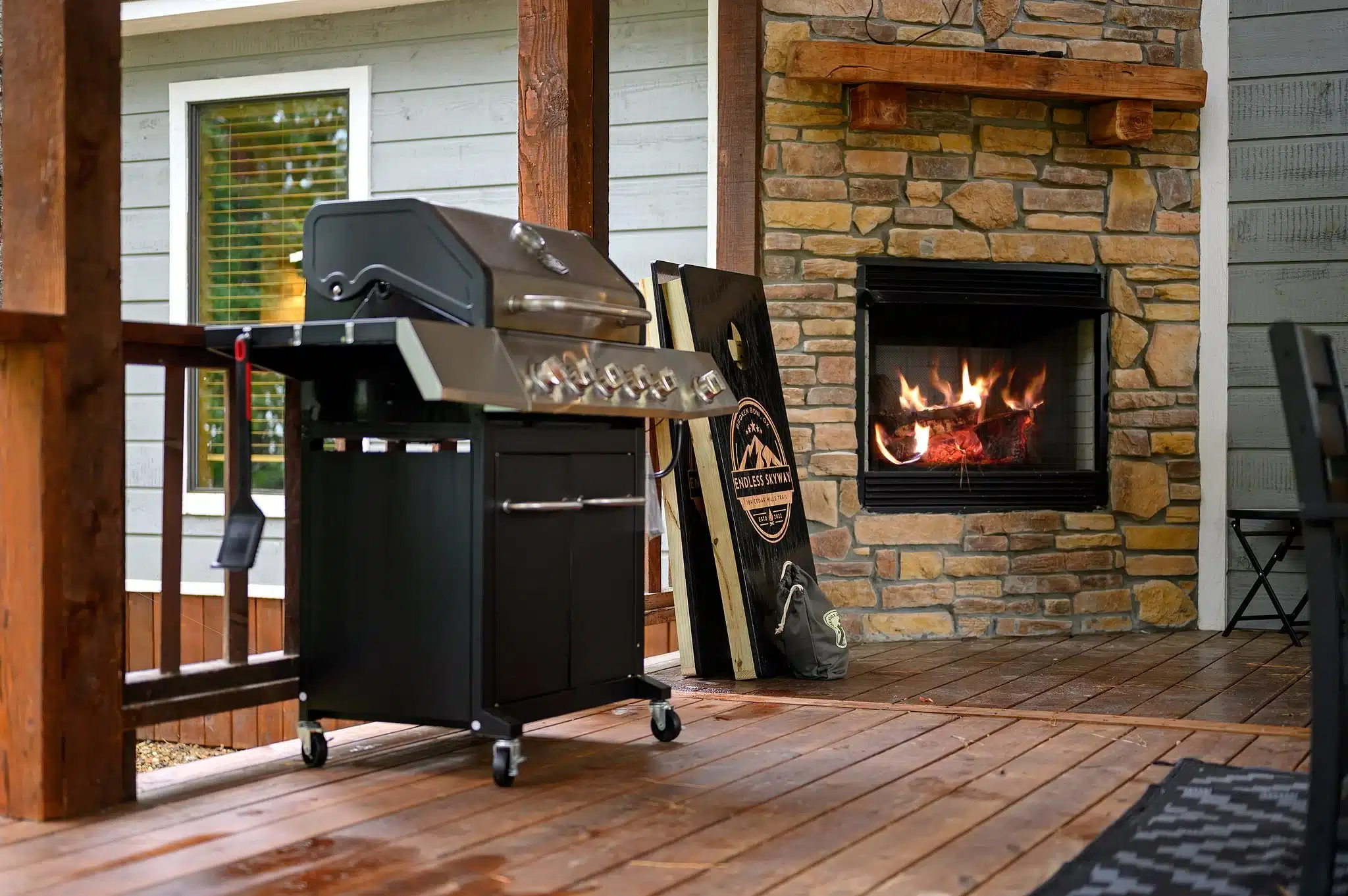 Covered patio with fireplace featuring stone walls, active fire, and stainless steel gas grill at Endless Skyway Cabin in