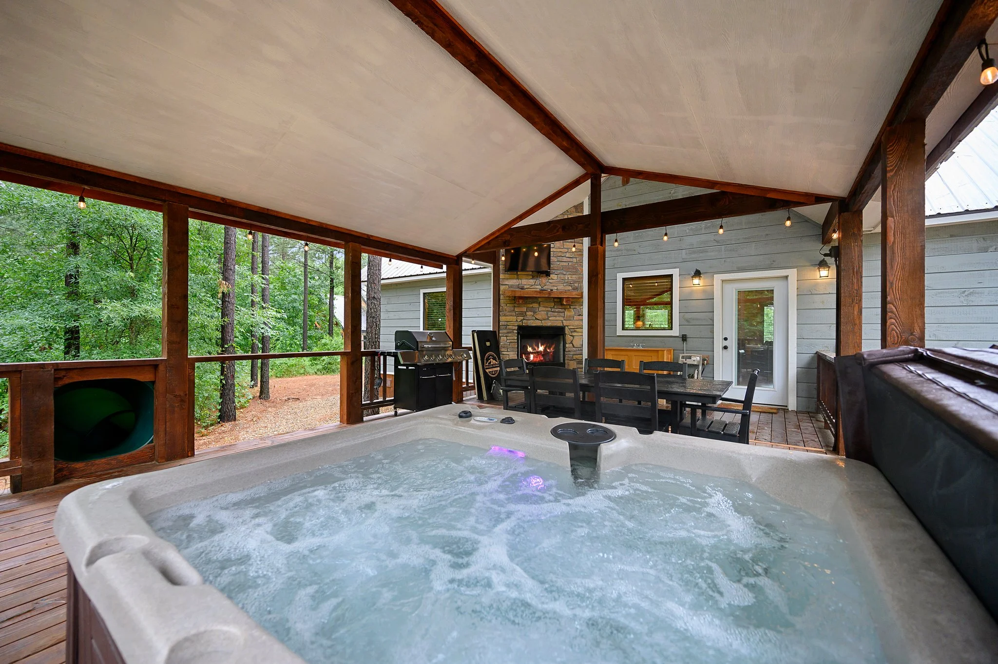 Covered patio at dusk with lit hot tub, stone fireplace and lounge chairs for relaxing evenings after Broken Bow brewery