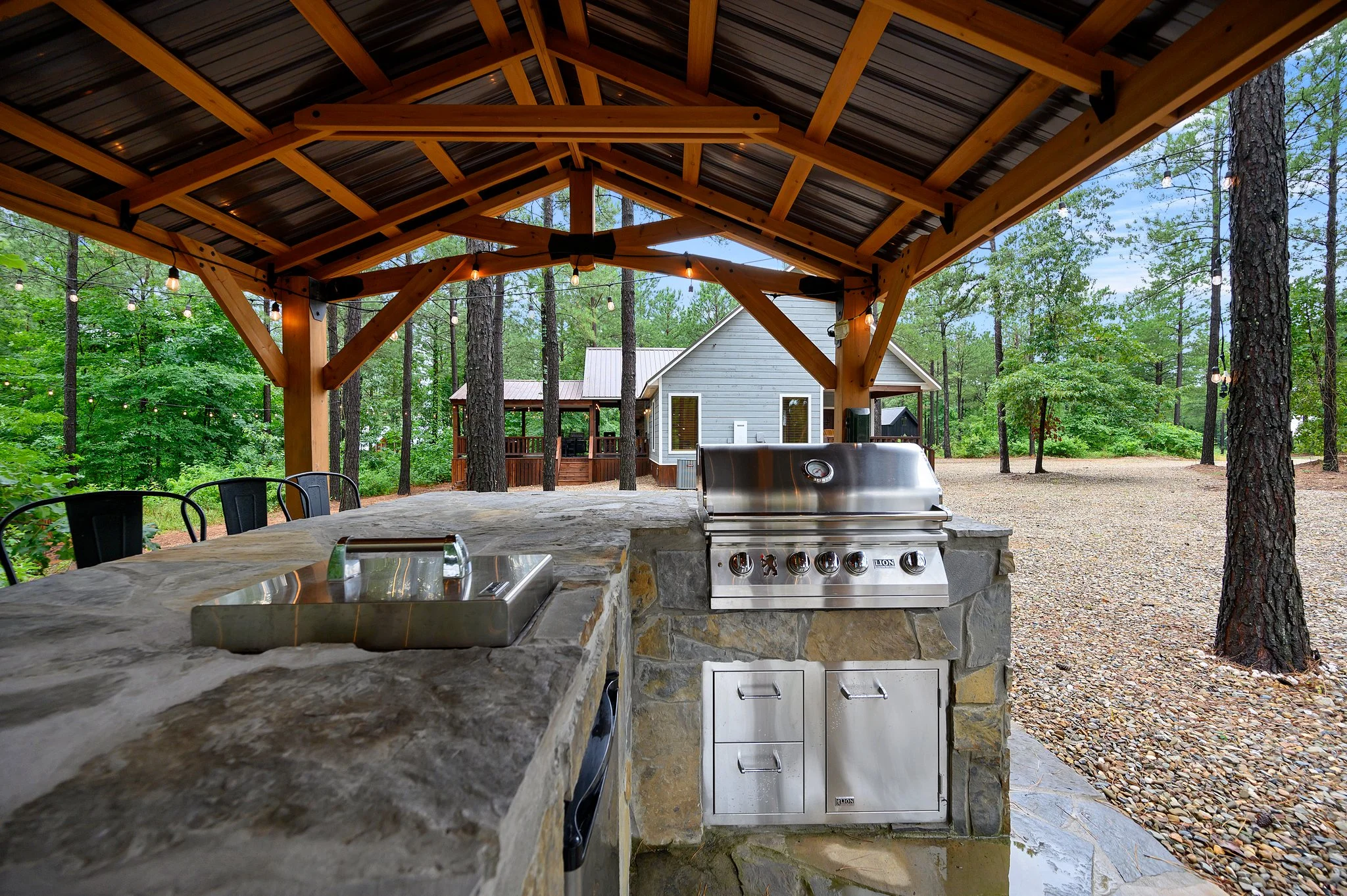 Covered wooden pergola patio with exposed timber beams, stone grill and counter, and pine forest views at Endless Skyway